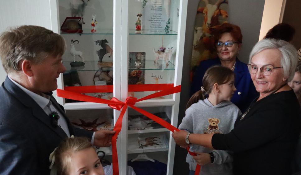 Przecięcie czerwonej wstęgi przy gablocie z kolekcją koziołków przez dzieci i dorosłych