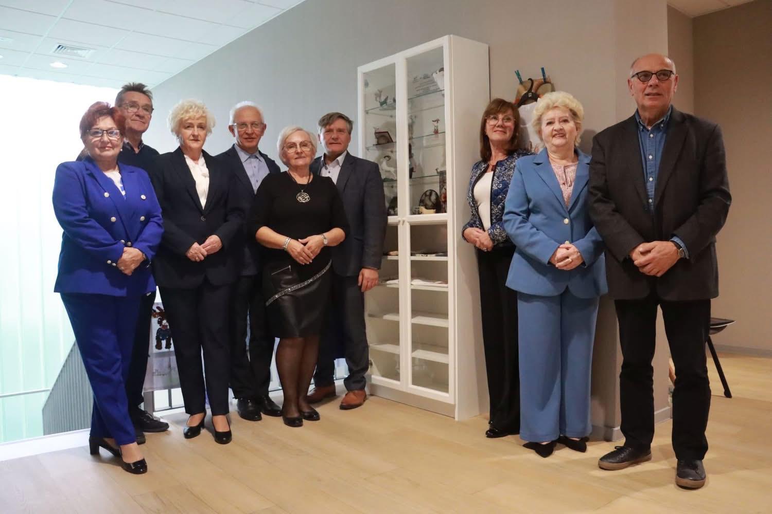 Grupa seniorów i organizatorów stojąca przy gablocie z koziołkami